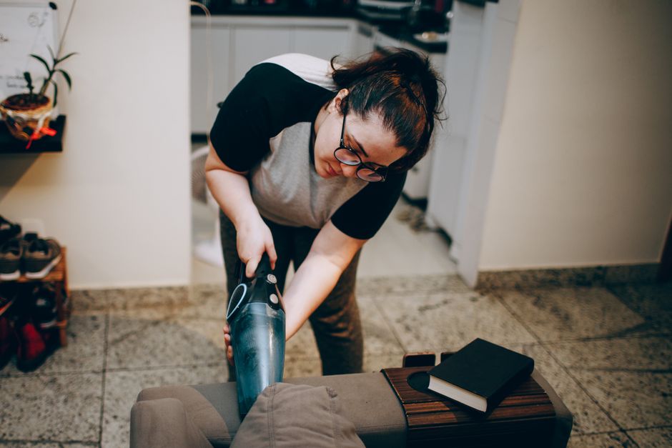 An adult woman vacuuming in a cozy living room with books on the sofa in a modern apartment.