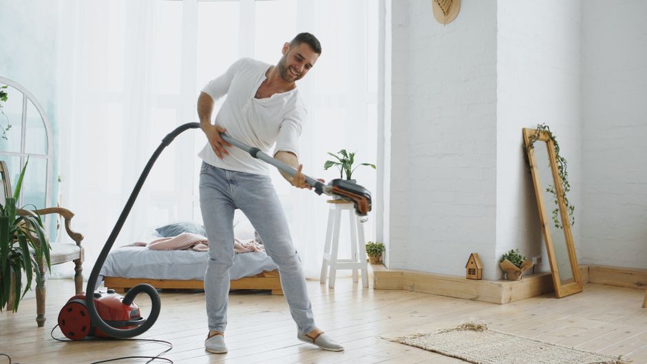 A smiling man cleans his stylish bedroom with a vacuum, creating a lively and fun atmosphere.